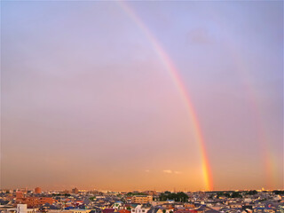 夕方の町に二重の虹が足を下ろしている風景
