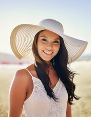 A woman in a summer setting, holding a wide-brimmed hat on a sunny beach. The image evokes feelings of relaxation and holiday