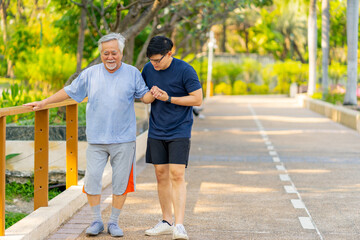 Elderly man suffering knee pain during jogging exercise with his son at park. A man support father...
