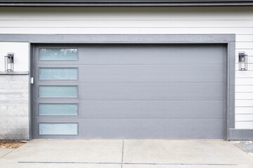 New modern gray garage door with glass panels on a light cream colored house with cement driveway

