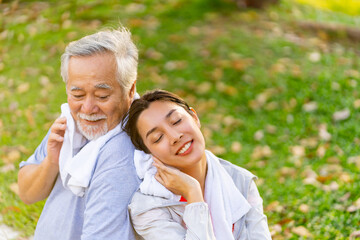 Asian woman daughter and elderly father resting after jogging exercise together at park. Retired man enjoy outdoor lifestyle sport workout in city. Family relationship and Senior people health care.