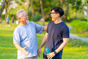 Happy Asian adult son and elderly father jogging exercise together at park. Retired man with...