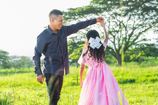 Latin father holding his daughter by the hand to give her a twirl on her own while looking at her proudly and smiling