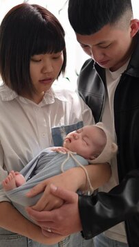 Vertical slow-motion video of a Taiwanese mother and father in their 20s standing and toasing a baby girl who is 1 month old in front of the curtain
20代の台湾人の母親と父親が生後１ヶ月の女の子の赤ちゃんをカーテンの前で立ってあやしている縦長スローモ
