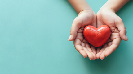 A pair of human hands gently cradling a vibrant red heart symbol on blue background with copy space.