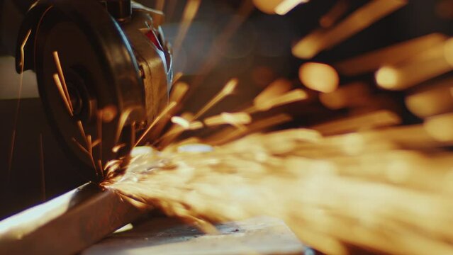 Angle grinder disk cutting metal workpiece and producing fire sparks in smithy. Close-up view