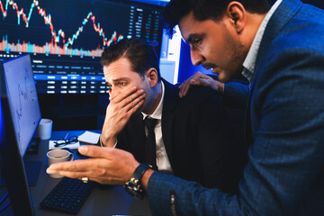 Stressful two stock investors with disappointed face focusing on dynamic currency market graph in...