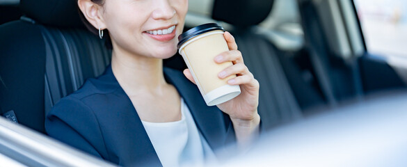 車内の運転席でコーヒーを持つスーツを着た女性