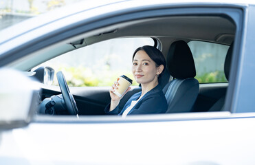 車内の運転席でコーヒーを持つスーツを着た女性