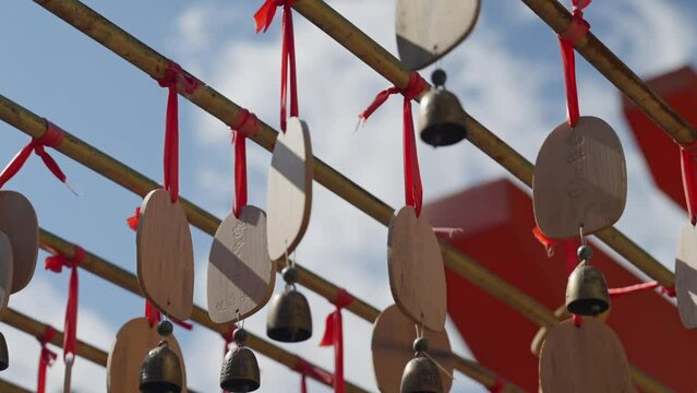 Rows of wish tags and bronze bells, hung on bamboo structures, symbolizing hopes and prayers in an Asian cultural setting under a clear sky.