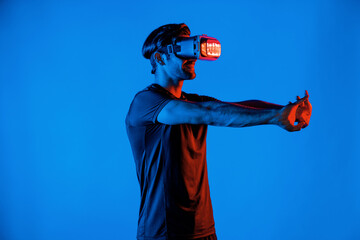 Happy man with VR goggle exercising and stretching arm at neon light background. Caucasian person...