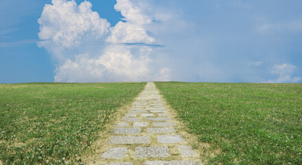緑の野原を貫く遠く地平線へ続く石畳の一本道　背景の青空と雲　アウトドア・夏・遠足・スタート・はじまりのイメージ背景　