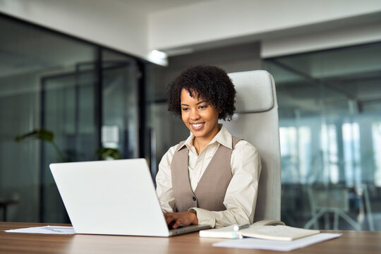 Professional happy business woman employee working on computer in office. Young busy African American businesswoman female company executive using laptop managing financial project sitting at desk.