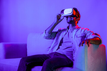 Man looking at VR glass to enter metaverse for watching movie and sitting at sofa with neon light....