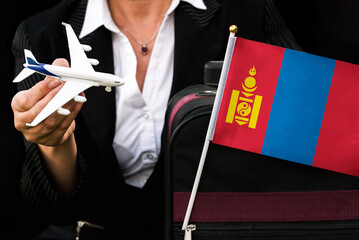 business woman holds toy plane travel bag and flag of Mongolia
