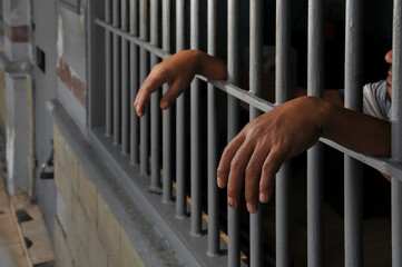 hands of a prisoner behind prison bars	