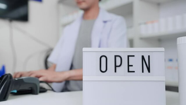 Pharmacist asian man holding lightbox with the inscription open on counter at pharmacy. Professional apothecary male working and sell medicine at drugstore. Healthcare and medical service concept