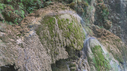 A fragment of a beautiful tropical waterfall. Streams flow down mossy openwork stone ledges. Water in the form of a veil. Philippines. Cebu. Tumalog Falls.  