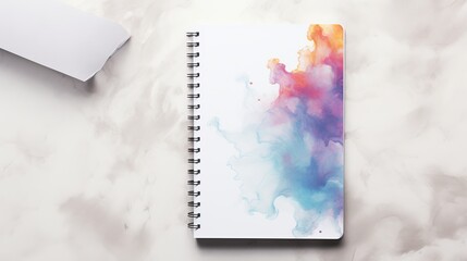An open notebook with a vibrant watercolor cover rests on a marble surface