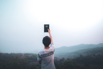 Man holding bible and lift up to the sky for pray for blessings to God.