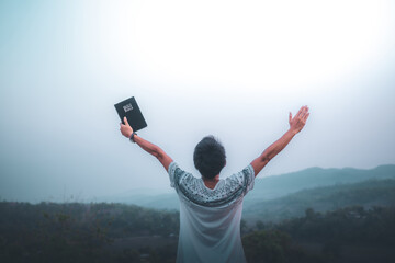 Man raised both hands up and holding bible, pray for blessings to God.