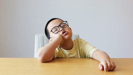 The glasses-wearing child sleeps with their chin resting on the table. isolated on white background