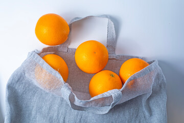 Fresh ripe oranges in a reusable shopping bag on a white background.