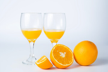 Two glasses of orange juice and a slice of orange on a white background.