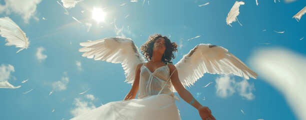 Mystical image of a woman with angel wings under a bright sun and floating feathers against a blue sky.
