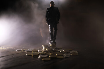 A miniature man standing in front of two paths with a stack of coins of different heights.