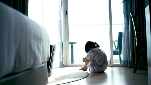 Squat single child sit near window, sad lonely in the room, crying, bad mood, offended, concept of unhappy childhood.