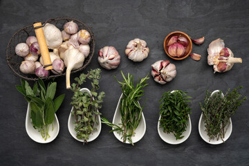 Fresh herbs in porcelain bowls, fresh garlic in a metal basket and on a large slate plate