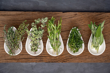 Five different fresh organic herbs in porcelain bowls on a rustic old wooden plank stand on a black...