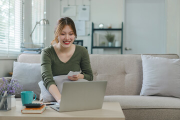 Smiling young asian woman working on laptop in bright living room.