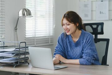 Focused young Asian businesswoman sitting and remote working on laptop computer in a modern home...
