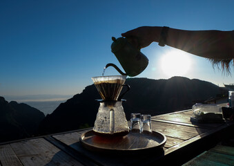 Closed up hand of barista pouring hot water from the kettle on coffee ground with filter, on wooden...