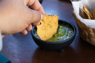 personal view of hand putting corn chips in green spicy sauce