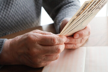 机上で紙幣を持つ高齢女性の手元と通帳