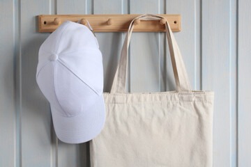 cloth bag and a white blank baseball cap hang on a wooden hanger on the wall, close-up. no plastic,...