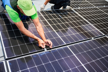 Worker building photovoltaic solar panel system on rooftop of house. Close up of man engineer...