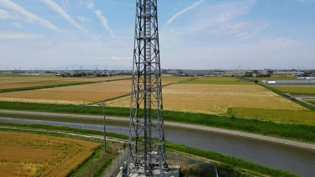 田園風景の中に立つ携帯電話基地局鉄塔　空撮でのパンアップ動画