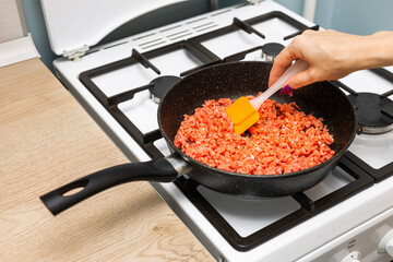 housewife frying fresh minced meat in a frying pan.