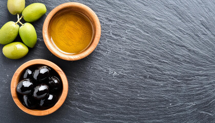 Black and green olives and oil in wooden bowl on black slate background. Top view with space for text.
