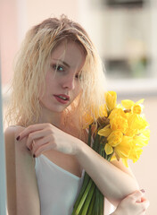 Junge Frau mit langen blonden Haaren mit einem Strauß Osterglocken. 