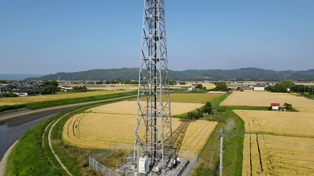 田園風景の中に立つ携帯電話基地局鉄塔　空撮でのパンアップ動画