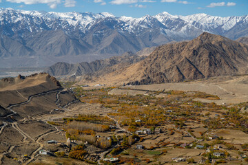 Spectacular high roads wind through rugged mountains beneath blue skies and the remote snow-capped peaks of Ladakh, India.