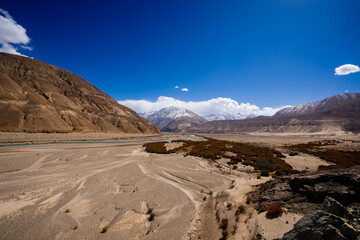 Vibrant view of the Indus River flowing through a barren Himalayan valley under a clear blue sky in Ladakh, India.