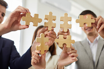 Happy smiling group of business people assembling wooden puzzle standing in office. Company...