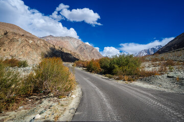 Spectacular high roads wind through rugged mountains beneath blue skies and the remote snow-capped peaks of Ladakh, India.
