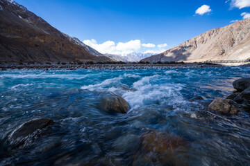 Vibrant view of the Indus River flowing through a barren Himalayan valley under a clear blue sky in...